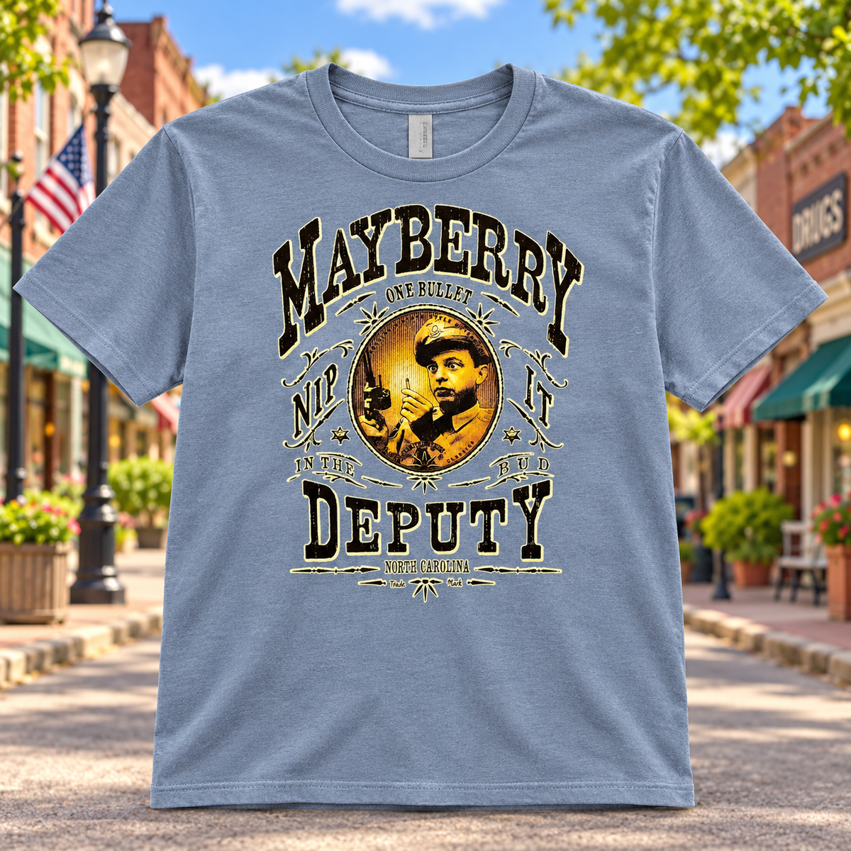 Mayberry One Bullet Deputy T-Shirt in Heather Blue against a bright Mayberry Main Street background