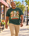 Man wearing Mayberry The Loaded Goat T-Shirt – Heather Forest Green walking on a Mayberry-inspired Main Street