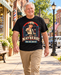 Man wearing Mayberry The Big House T-Shirt – Black walking on a Mayberry-inspired Main Street