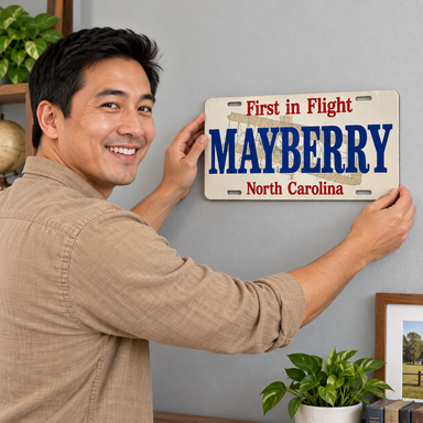 Man placing Mayberry Metal Sign - First in Flight on a wall