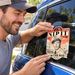 Man applying the Mayberry Nip It in the Bud sticker to his car's rear side window.